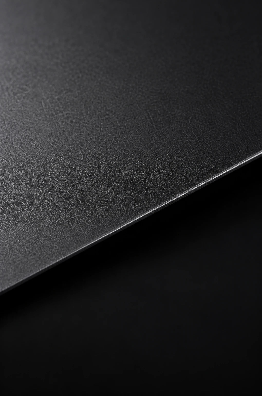 Thin anodised aluminium sheet material study, with a fine-grained charcoal surface and a crisp diagonal edge.