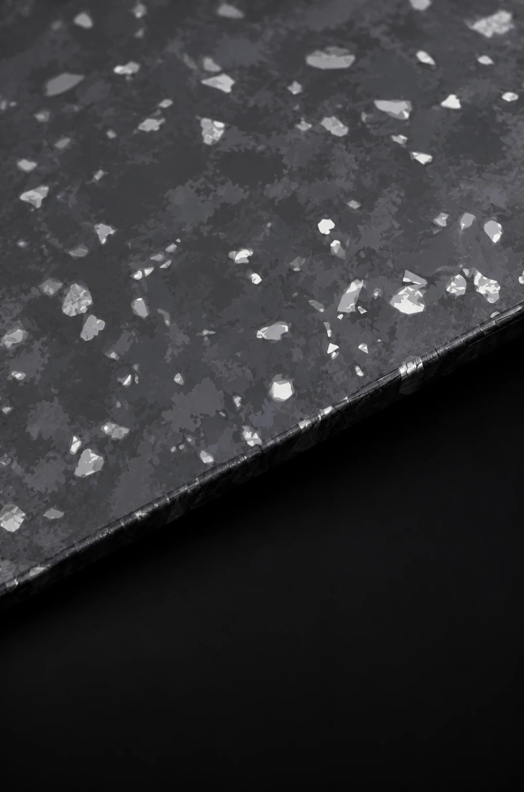 Argento forged-carbon sheet material study, with layered charcoal markings, irregular silver fragments and a thin diagonal edge.