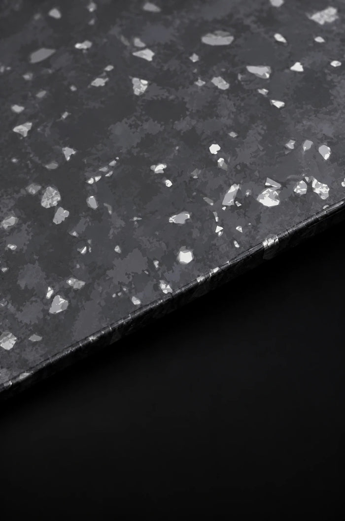 Close-up material study of forged carbon with irregular silver-coloured fragments